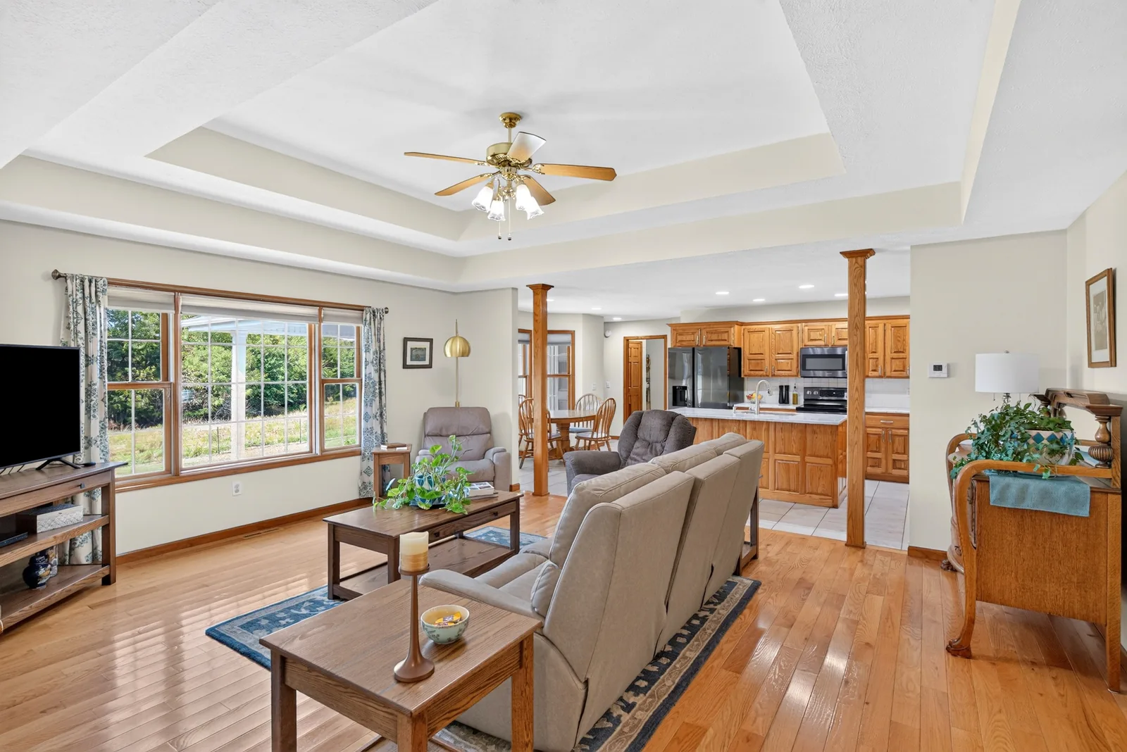 Living room with a tray ceiling, hardwood floors and a wall of windows, open to the kitchen