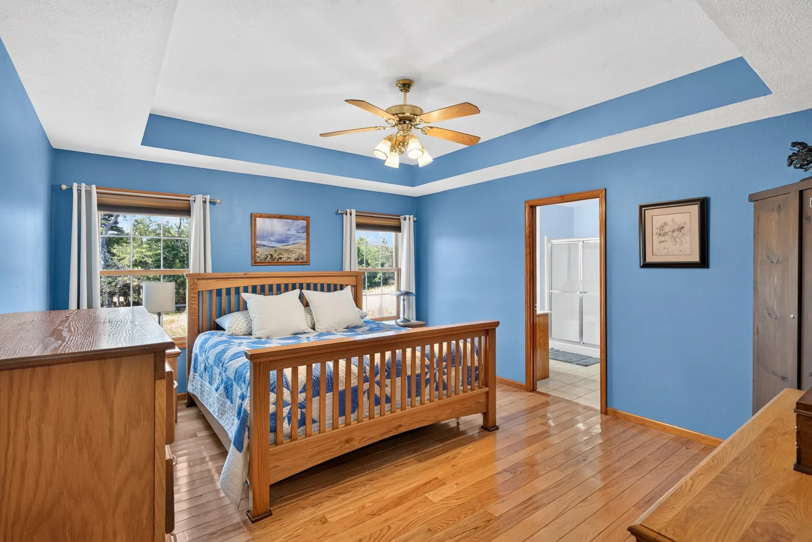 Blue primary bedroom with a tray ceiling, hardwood floors and a door to the primary bath