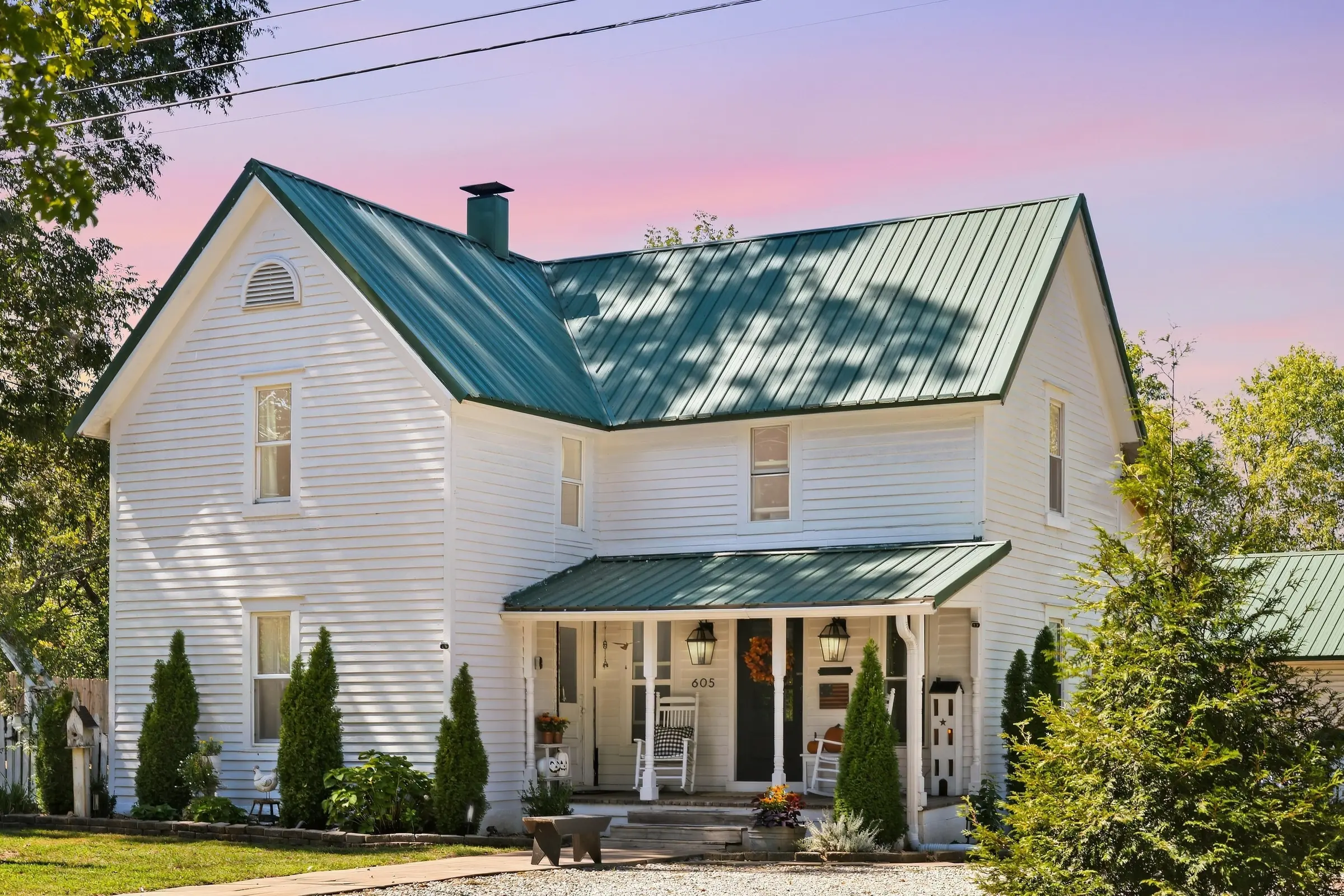Twilight exterior of a white two-story farmhouse with a green metal roof