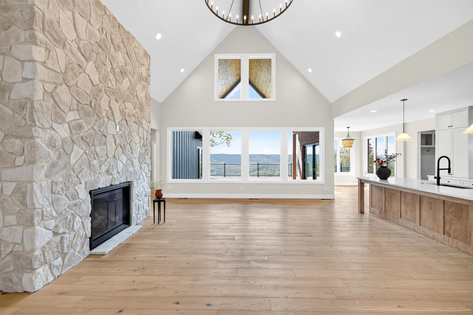 Vaulted great room with a stone fireplace and a wall of windows over the hills