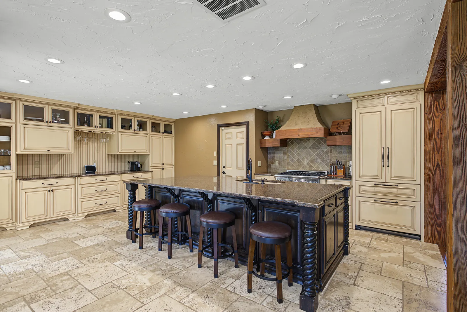 Kitchen with a large dark island, cream cabinetry and travertine floors
