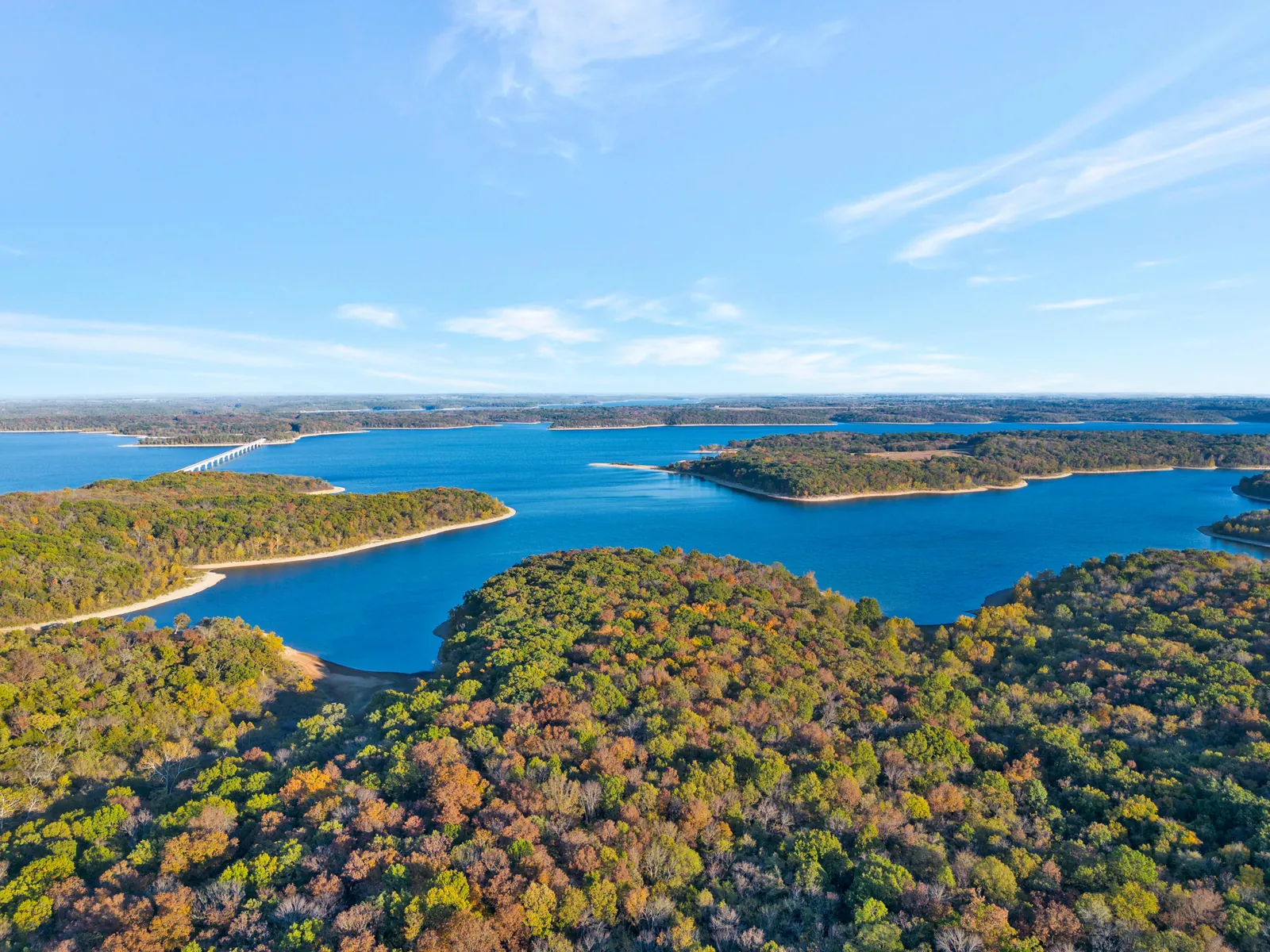 Aerial view of a lake winding through wooded hills in early fall